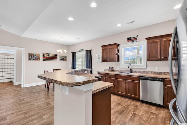 kitchen featuring appliances with stainless steel finishes, pendant lighting, sink, a kitchen bar, and light wood-type flooring