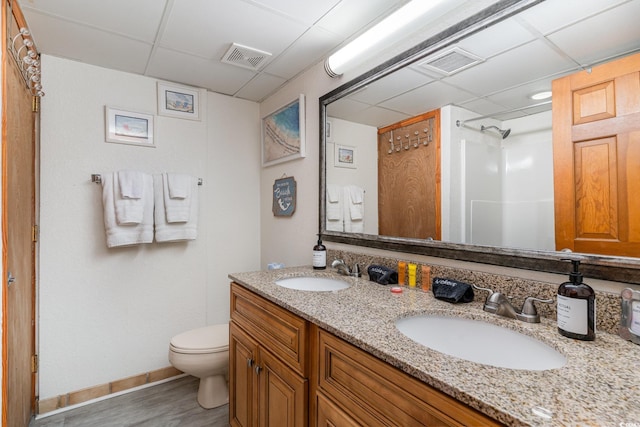 bathroom with toilet, a shower, vanity, hardwood / wood-style floors, and a drop ceiling