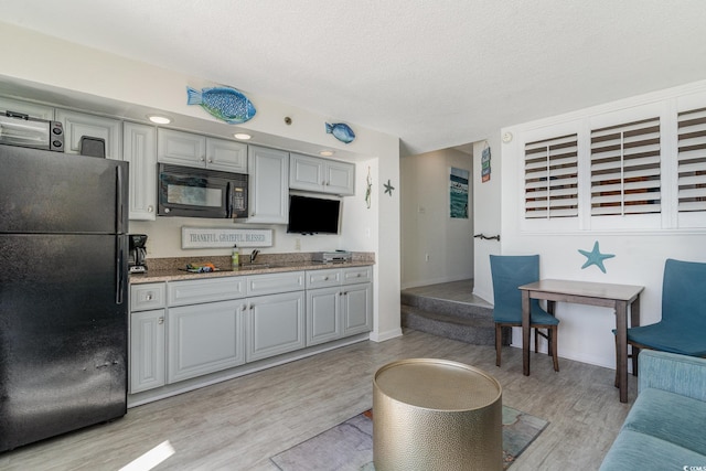 kitchen featuring gray cabinetry, a textured ceiling, light hardwood / wood-style flooring, and black appliances