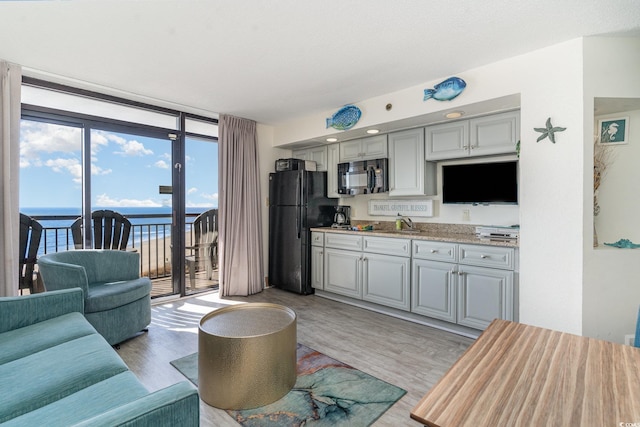 kitchen with gray cabinets, a water view, expansive windows, and black appliances