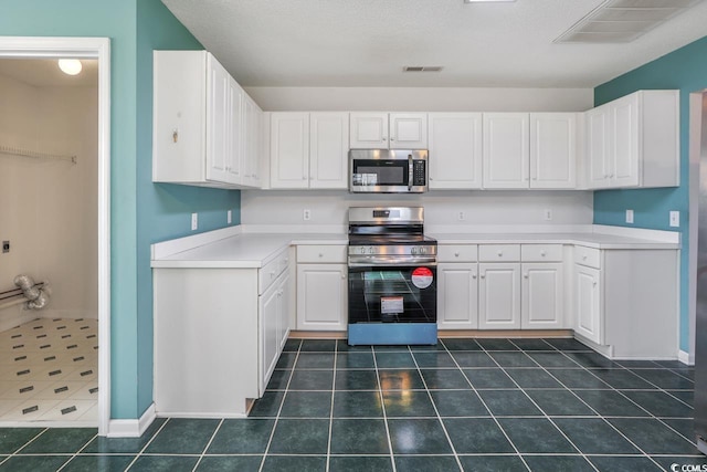 kitchen featuring dark tile patterned floors, a textured ceiling, white cabinets, and appliances with stainless steel finishes