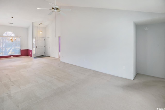 carpeted empty room featuring ceiling fan with notable chandelier and high vaulted ceiling