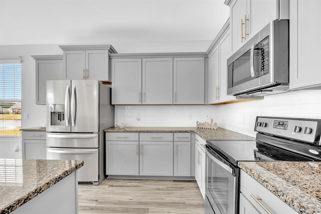 kitchen featuring light stone counters, backsplash, stainless steel appliances, and light hardwood / wood-style floors