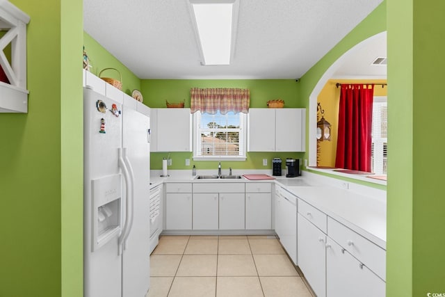 kitchen with light tile patterned floors, a sink, light countertops, white cabinets, and white refrigerator with ice dispenser