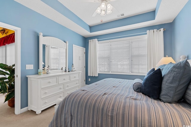 bedroom featuring a raised ceiling, a ceiling fan, visible vents, and light carpet