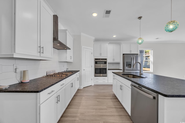 kitchen with stainless steel appliances, white cabinets, wall chimney range hood, decorative light fixtures, and sink