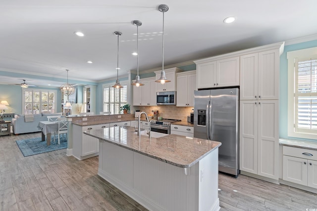 kitchen with stainless steel appliances, a kitchen island with sink, pendant lighting, and white cabinets