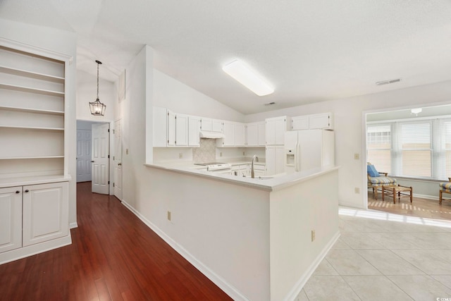 kitchen featuring sink, white cabinetry, white refrigerator with ice dispenser, decorative light fixtures, and vaulted ceiling