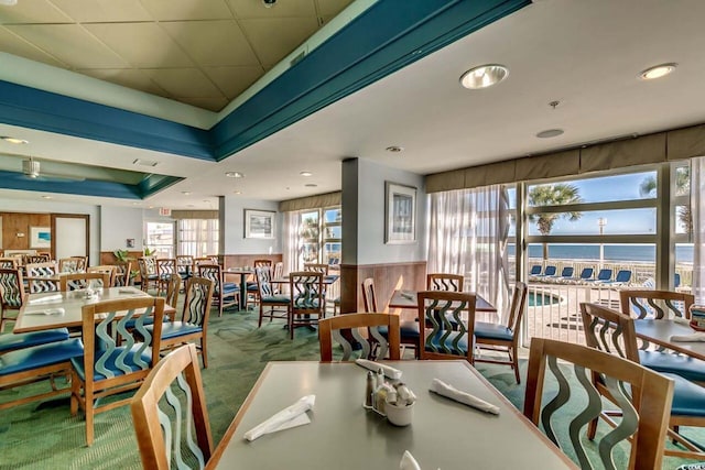 dining area featuring a water view, a raised ceiling, and carpet floors