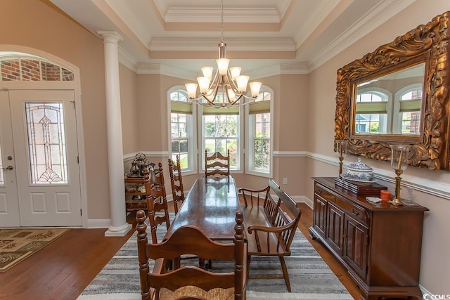 dining space featuring decorative columns, dark hardwood / wood-style flooring, a notable chandelier, a tray ceiling, and crown molding