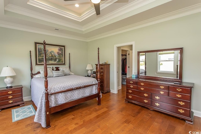 bedroom with a closet, a spacious closet, wood-type flooring, and a raised ceiling