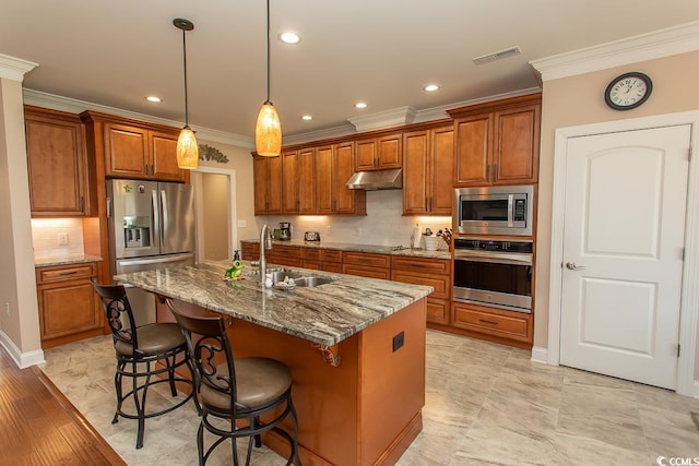 kitchen with appliances with stainless steel finishes, stone countertops, decorative light fixtures, an island with sink, and sink