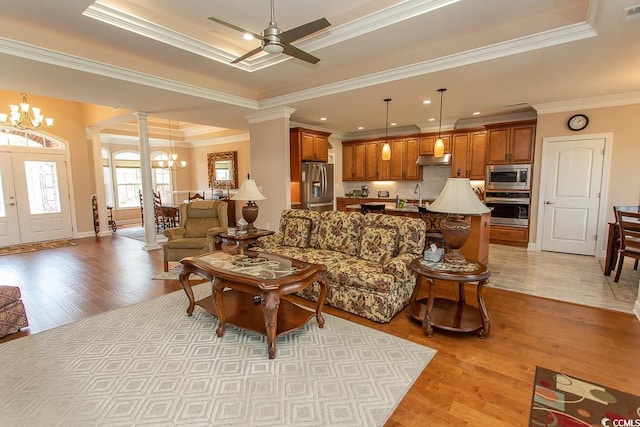 living room with ornate columns, sink, a tray ceiling, crown molding, and light wood-type flooring