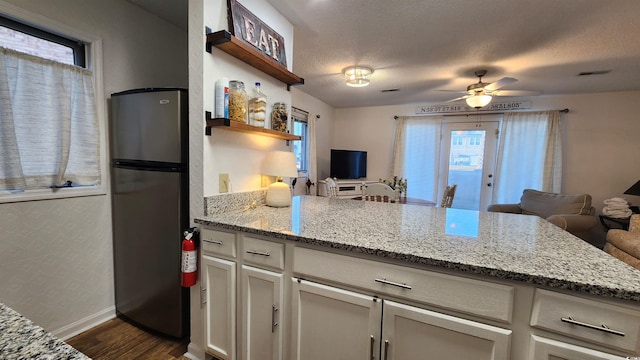 kitchen with white cabinetry, stainless steel fridge, light stone countertops, and a textured ceiling