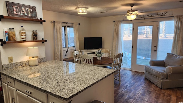 kitchen featuring light stone counters, ceiling fan, dark wood-type flooring, and a textured ceiling