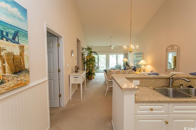 kitchen featuring pendant lighting, sink, white cabinetry, high vaulted ceiling, and light colored carpet