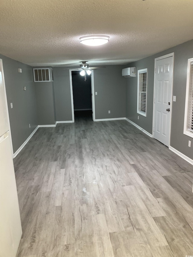 spare room with a textured ceiling, wood finished floors, visible vents, baseboards, and a wall mounted AC