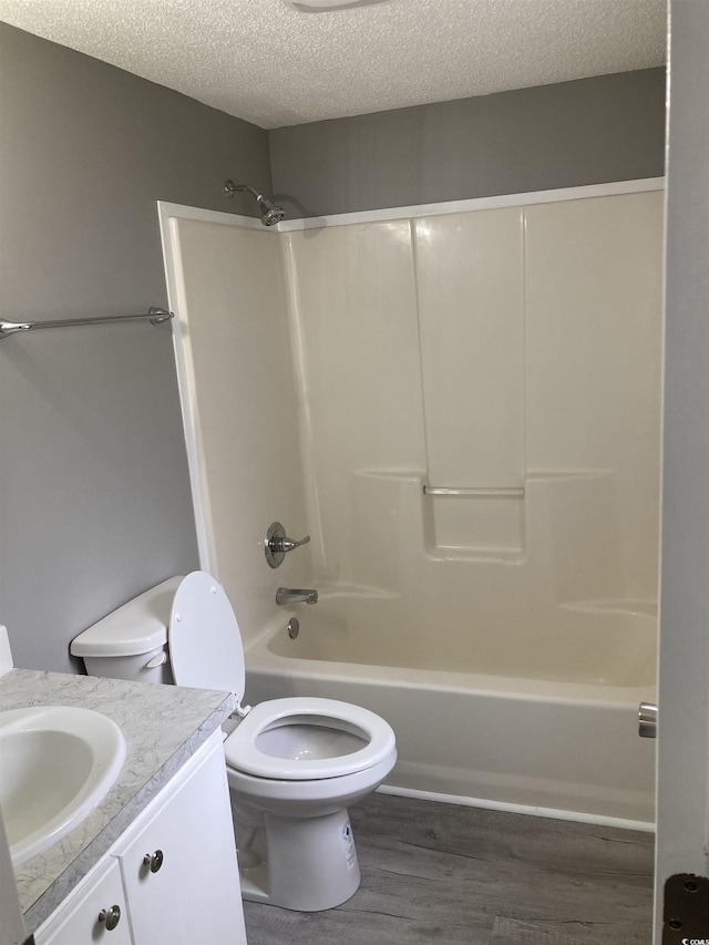 bathroom featuring a textured ceiling, toilet, wood finished floors, vanity, and bathing tub / shower combination