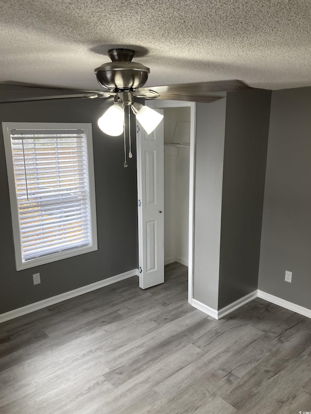 unfurnished bedroom with ceiling fan, a textured ceiling, baseboards, and wood finished floors