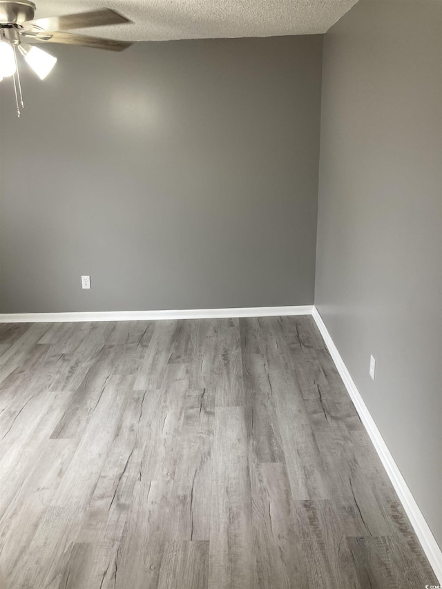 spare room with a textured ceiling, baseboards, and wood finished floors