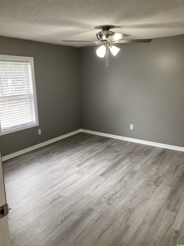 empty room featuring ceiling fan, a textured ceiling, baseboards, and wood finished floors