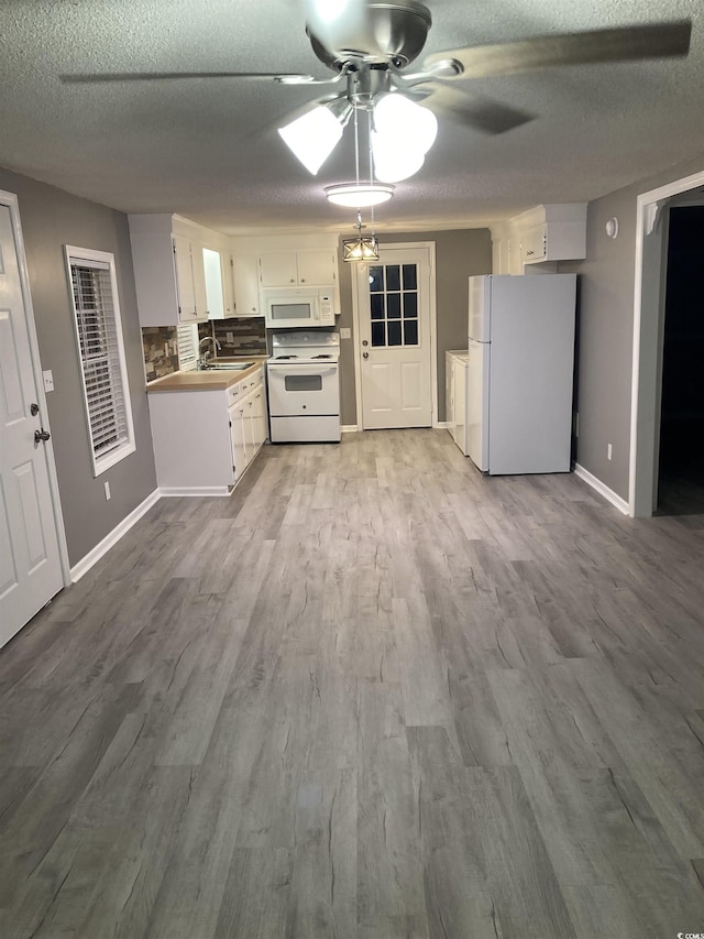 kitchen featuring a textured ceiling, white appliances, wood finished floors, white cabinetry, and decorative backsplash