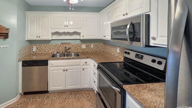 kitchen with sink, stone counters, appliances with stainless steel finishes, white cabinets, and light wood-type flooring