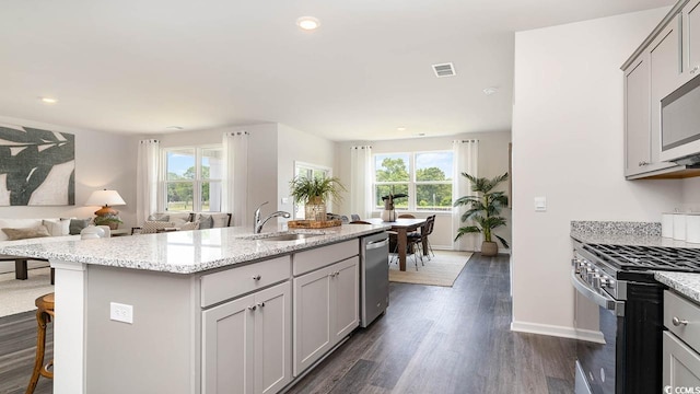 kitchen featuring sink, appliances with stainless steel finishes, a kitchen breakfast bar, light stone countertops, and a center island with sink