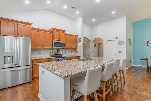 kitchen featuring sink, a breakfast bar area, appliances with stainless steel finishes, light stone countertops, and a kitchen island with sink