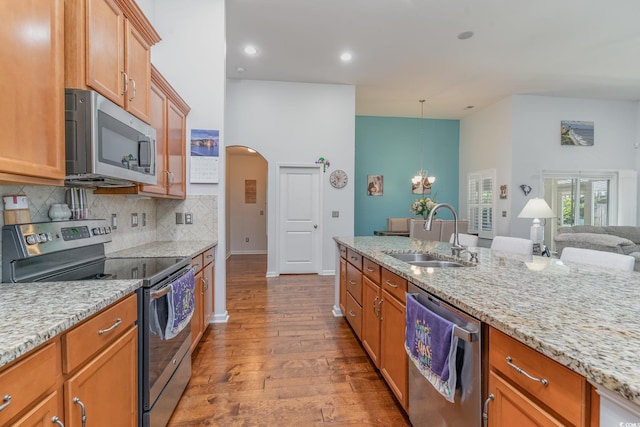 kitchen with pendant lighting, sink, stainless steel appliances, tasteful backsplash, and light stone countertops