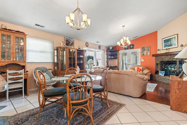 dining space featuring a brick fireplace, a notable chandelier, and light tile patterned floors