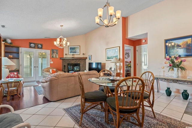 dining area featuring a brick fireplace, a chandelier, vaulted ceiling, and light tile patterned flooring