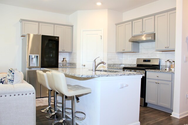 kitchen with gray cabinetry, light stone counters, stainless steel appliances, and a center island with sink