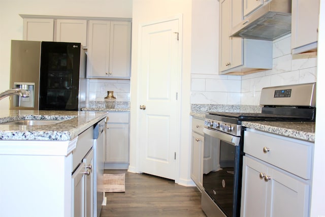 kitchen featuring appliances with stainless steel finishes, sink, dark hardwood / wood-style flooring, decorative backsplash, and light stone counters