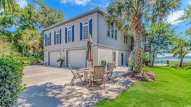 back of house with a water view, a garage, and a lawn