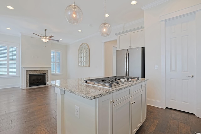 kitchen featuring light stone counters, dark wood-style floors, stainless steel appliances, a fireplace with flush hearth, and ornamental molding