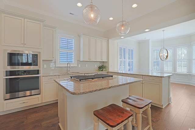 kitchen with a center island, a peninsula, stainless steel appliances, crown molding, and a sink