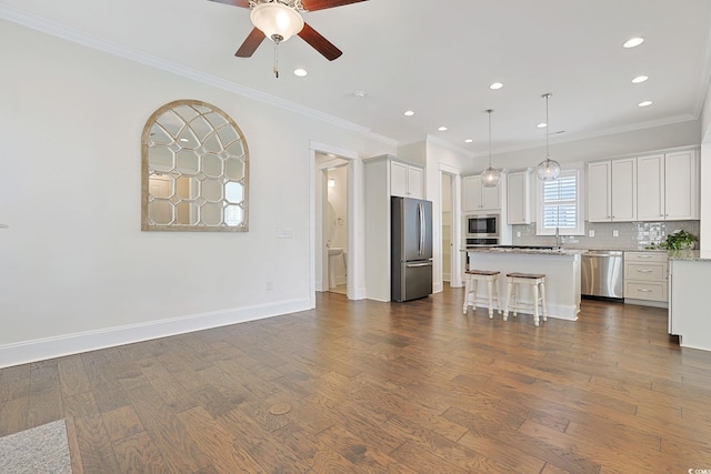 kitchen with ornamental molding, appliances with stainless steel finishes, dark wood-style flooring, and a center island