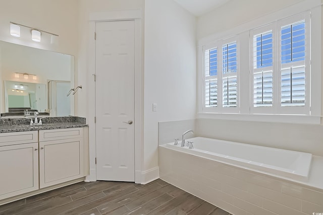 full bath with wood finish floors, a garden tub, vanity, and baseboards