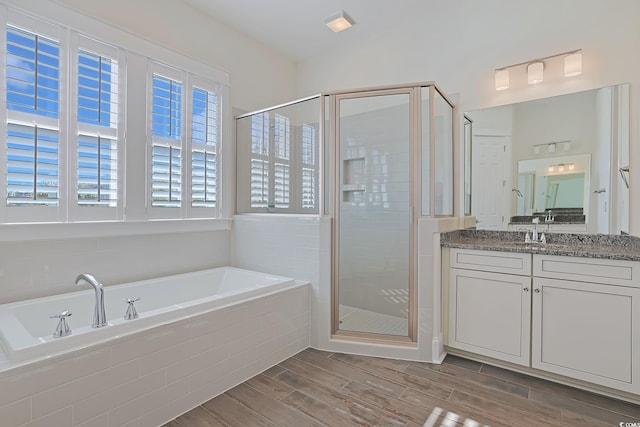 full bath featuring wood finish floors, a garden tub, a shower stall, and vanity