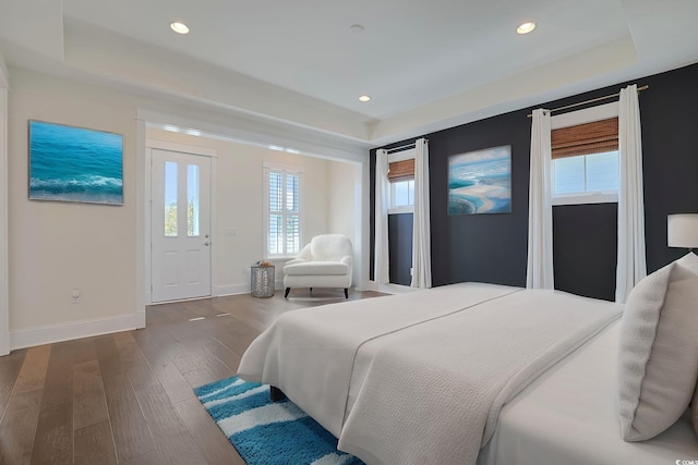 bedroom featuring wood finished floors, recessed lighting, a raised ceiling, and baseboards