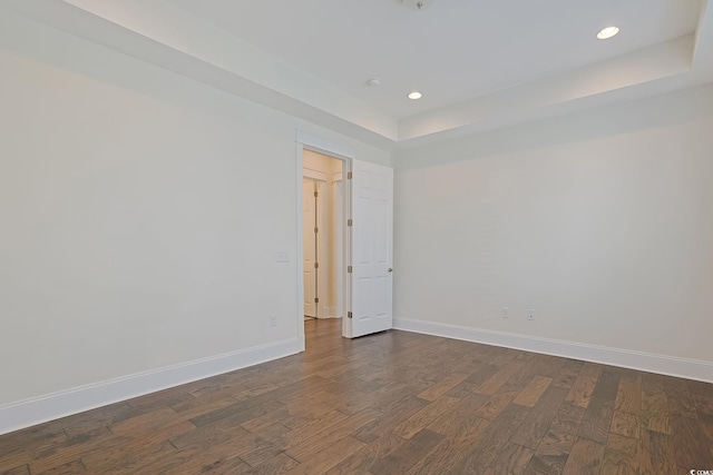 empty room with dark wood-style floors, a tray ceiling, recessed lighting, and baseboards