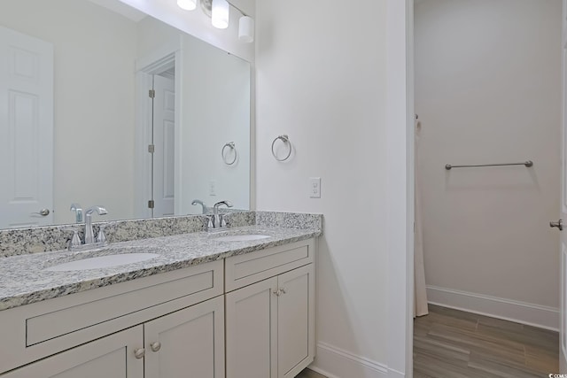 bathroom with wood finished floors, a sink, baseboards, and double vanity