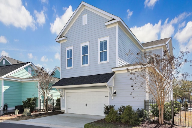 traditional-style house featuring a garage, driveway, a shingled roof, and fence