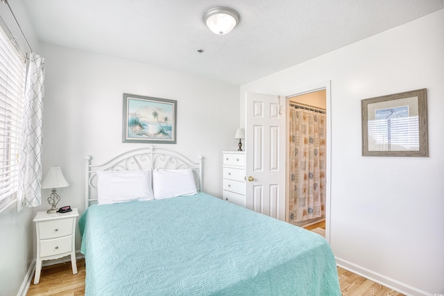 bedroom with connected bathroom, a textured ceiling, and light wood-type flooring