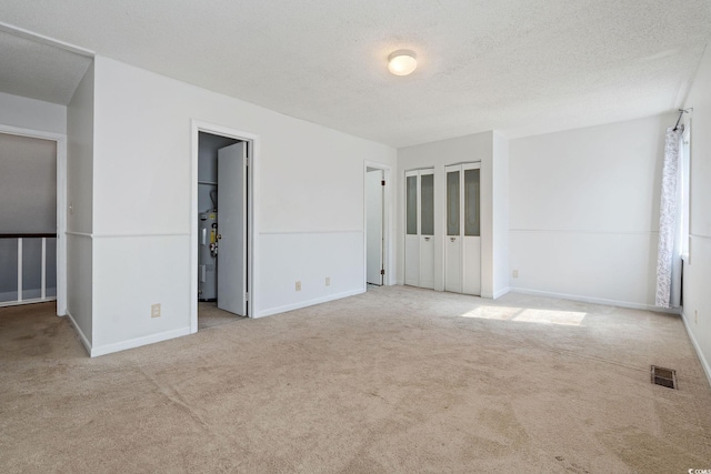 spare room with water heater, light carpet, and a textured ceiling