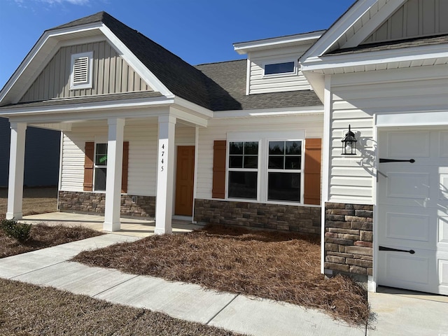 property entrance with a garage, covered porch, stone siding, roof with shingles, and board and batten siding