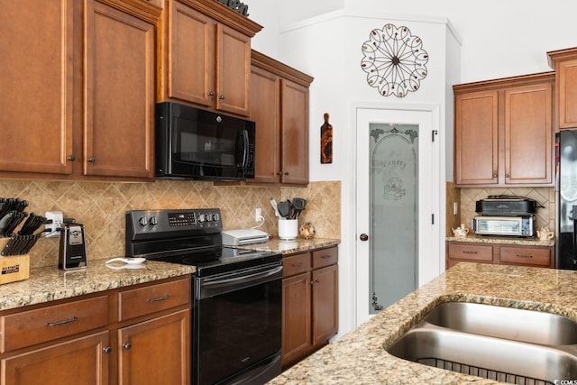 kitchen with tasteful backsplash, light stone countertops, black appliances, and sink