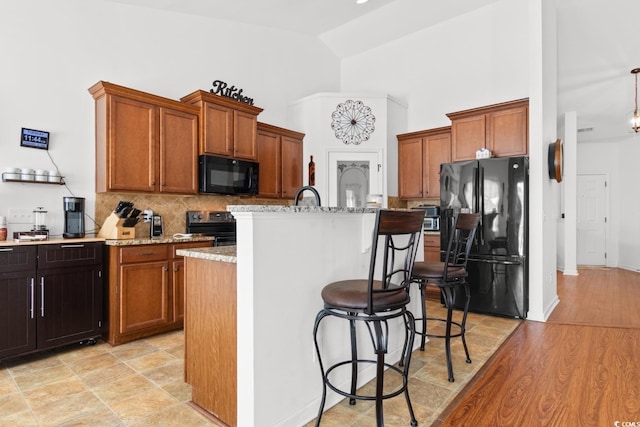 kitchen featuring high vaulted ceiling, tasteful backsplash, black appliances, light stone countertops, and a center island with sink