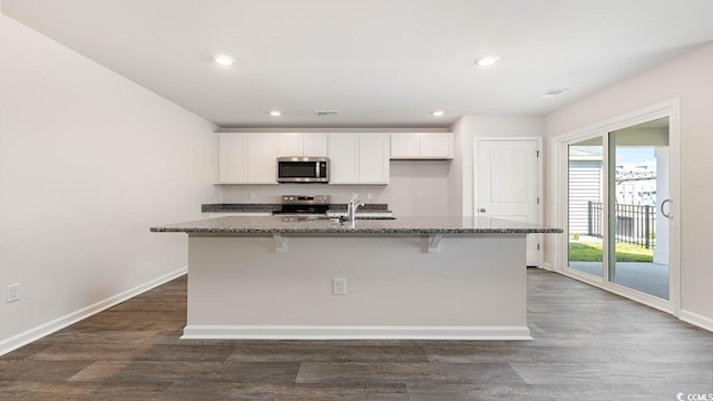 kitchen with a center island with sink, stainless steel appliances, stone countertops, dark wood-type flooring, and white cabinets